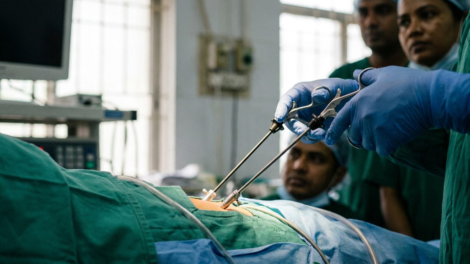 Close up of gloved hands using laparoscopic graspers during stepwise surgical training in a Dhaka operating theatre.