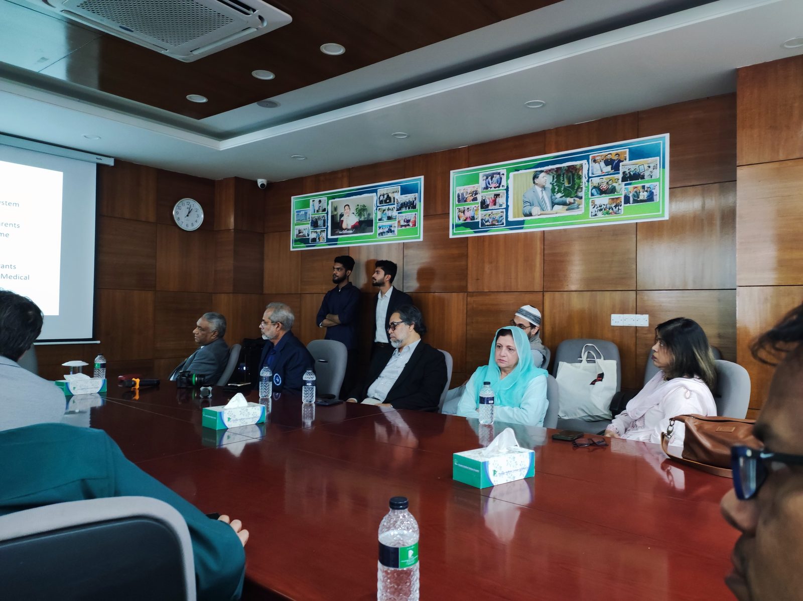 Thirteen participants attending a medical presentation on supervised surgical training in a wood-paneled conference room.